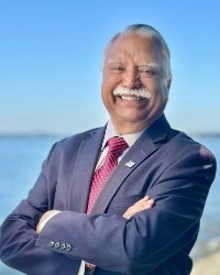 Satpal Singh Sidhu smiles wearing a tie and standing on the beach.