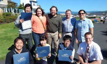 A group of International students stand outside holding their diplomas at Marine Park.