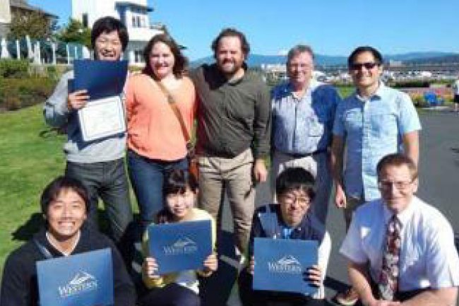 A group of International students stand outside holding their diplomas at Marine Park.