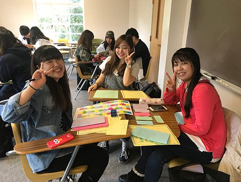 3 auap students sit in a classroom doing an art project