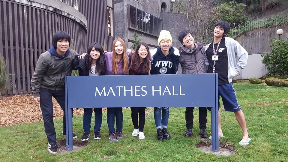 Group of AUAP WWU students stand smiling behind a large blue sign of Mathes Hall