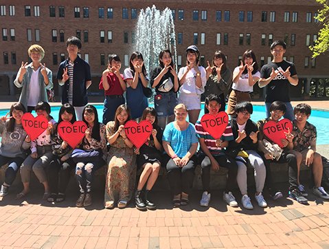 group of AUAP students sitting in front of the fountain in red square while holding heart shaped posters saying "TOEIC" on them.
