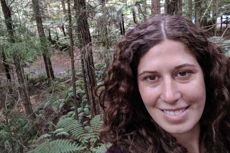  Molly, with long brown curly hair and brown eyes, takes a selfie in the woods