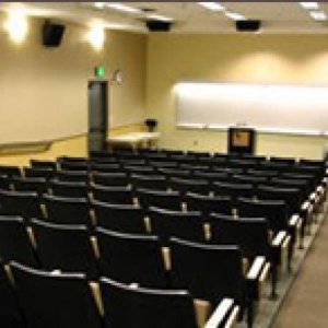 An empty classroom full of empty seats faces the podium at the front of the class.