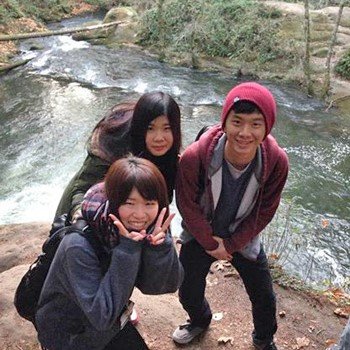 Three international students pose for the camera outside in nature, alongside a river