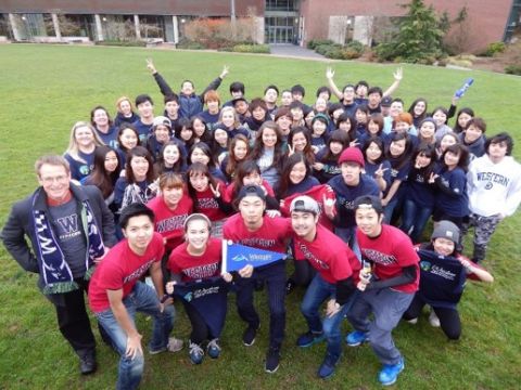 Group of WWU-AUAP students in matching red and blue t-shirts stand outside on the campus lawn in a celebratory pose.