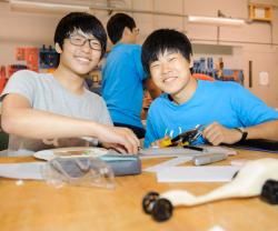 Two male youth students working on model race cars in a classroom