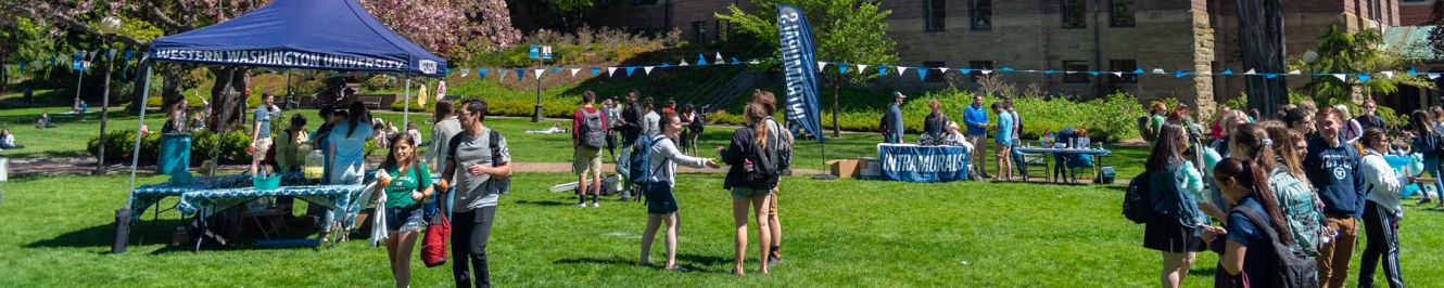 Students gather on the lawn for a summer festival amid blue WWU tents.
