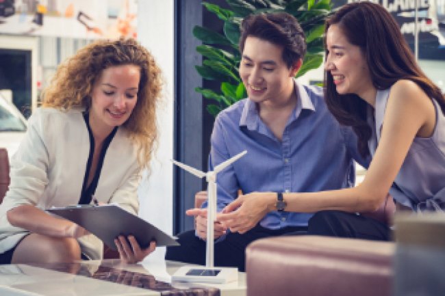 Three people work together on a energy policy. A model of a windmill sits on the table in front of them.