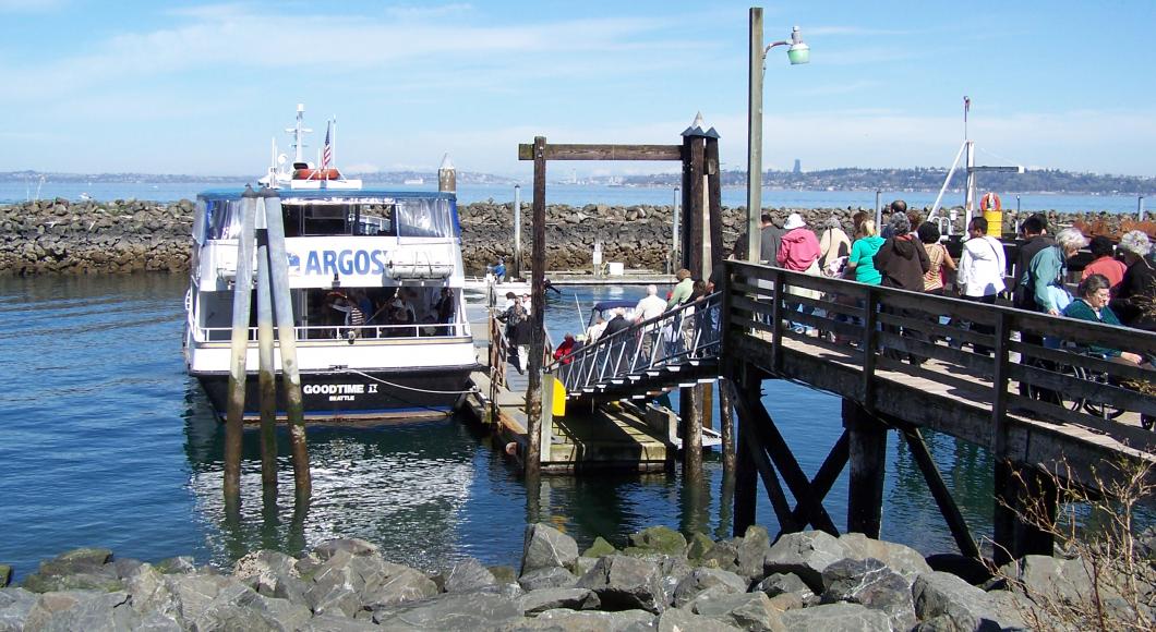 A line forms on a dock as people line up to get on a medium sized boat.